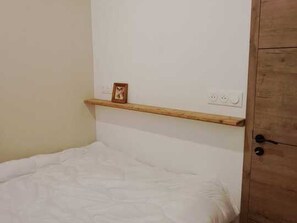 Ein Einzelbett mit Holz Kopfteil, ein kleines Regal mit Bilderrahmen und eine Tür mit schwarzem Griff.