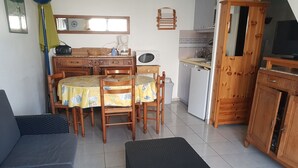 Kompakti oleskelutila, jossa on ruokapöytä, tuoleja, sohva, pieni jalkarahi, pieni keittiö ja televisio.