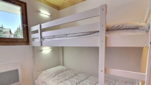 Ein Schlafraum mit Etagenbetten, einem Fenster, einer Holzzieldecke und einer weißen Wand.