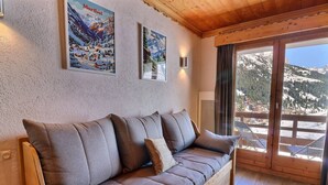 Ein Sofa mit Holzrahmen und Kissen, eine Wand mit zwei gerahmten Bildern und ein großes Fenster mit Bergblick.