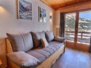 Ein Sofa mit Holzrahmen und Kissen, eine Wand mit zwei gerahmten Bildern und ein großes Fenster mit Bergblick.