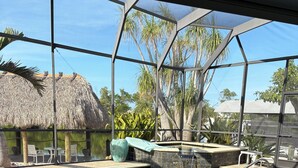 Un espace piscine avec une eau claire, une structure à toit de chaume et un coin salon avec des chaises et une table.