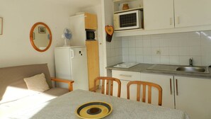 Une cuisine compacte équipée d’un four à micro-ondes, d’un petit réfrigérateur et d’un évier. On y trouve une table à manger avec des chaises, ainsi qu’une petite table ronde sur laquelle est posé un saladier.