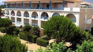 Un hôtel doté d’un toit recouvert de tuiles rouges, de nombreux balcons et d’un jardin agrémenté de diverses plantes.
