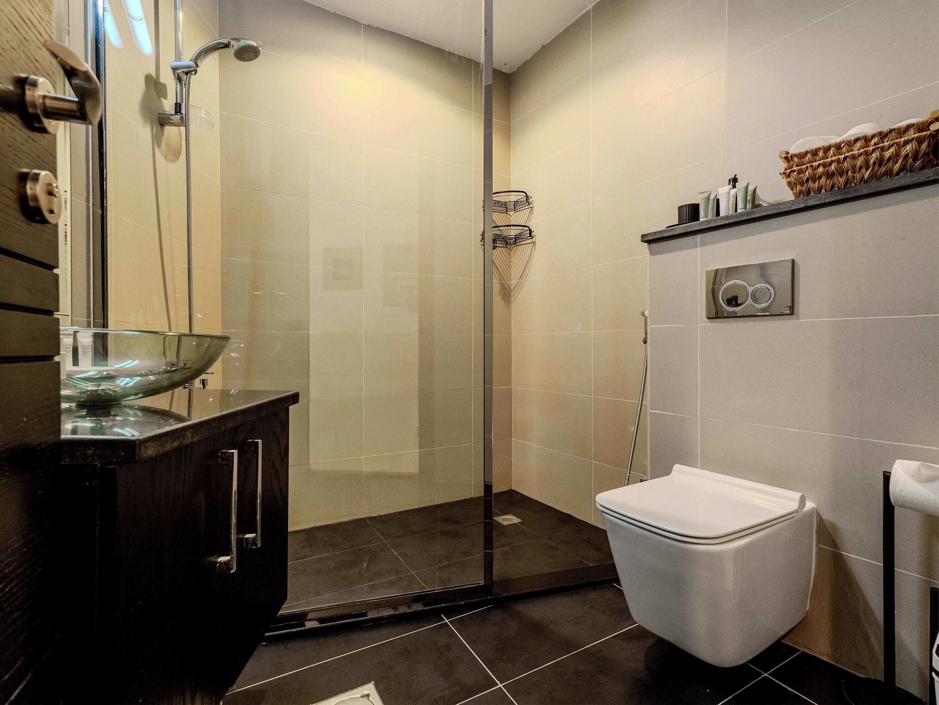 A modern bathroom with a glass-enclosed shower, a white toilet, and a dark wooden vanity with a glass bowl.
