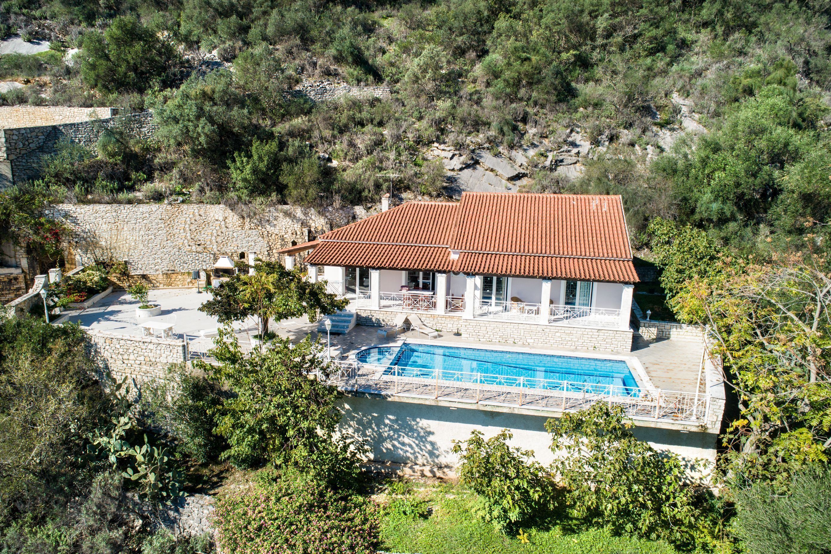 Una villa con piscina, muros de piedra y techo de tejas rojas.