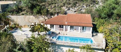 Una villa con piscina, muros de piedra y techo de tejas rojas.