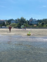 Una playa con agua cristalina, un flotador con forma de tortuga y edificios al fondo.