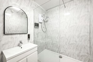 Un bagno moderno con parete in marmo bianco, un ampio specchio, un lavabo bianco e una cabina doccia in vetro.