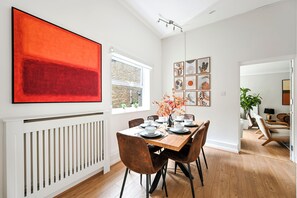 Zona pranzo con tavolo in legno apparecchiato per sei persone, pareti bianche e un grande quadro astratto sopra.
