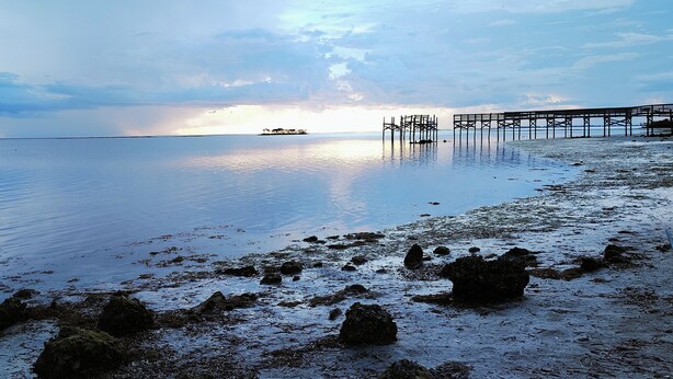 A calm beach with a pier extending into the water, rocky shoreline, and a distant boat. - Nostalgic 2bed home in Crystal River, Minutes to Kings bay, Manatees &more (Crystal River)