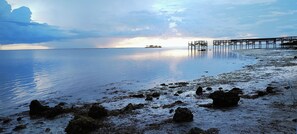 A calm beach with a pier extending into the water, rocky shoreline, and a distant boat. - Nostalgic 2bed home in Crystal River, Minutes to Kings bay, Manatees &more (Crystal River)