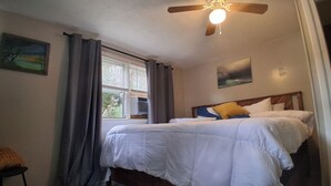 A bedroom with a bed, a ceiling fan, a window with curtains, and a painting on the wall. - Nostalgic 2bed home in Crystal River, Minutes to Kings bay, Manatees &more (Crystal River)