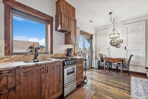 A kitchen with wooden cabinets, a stove, and a dining area with a table and chairs. - Downtown Whitefish Studio w/ Fireplace (Whitefish)