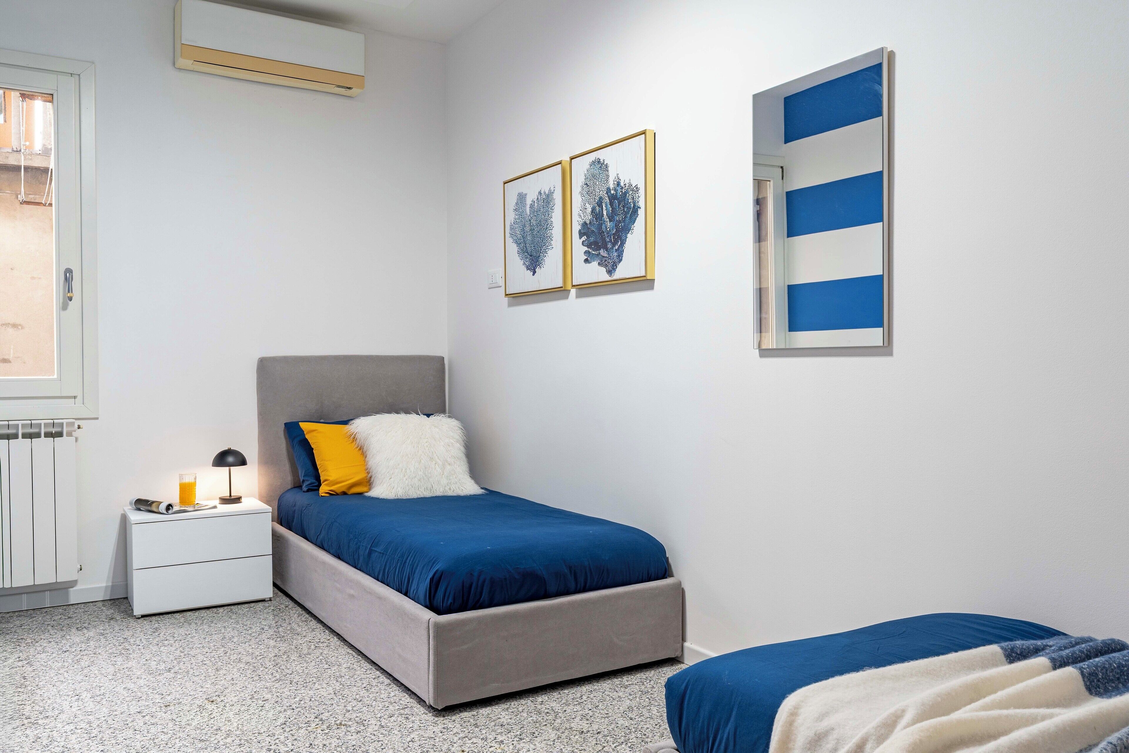 A bedroom with a bed, bedside table, lamp, and artwork on the wall.