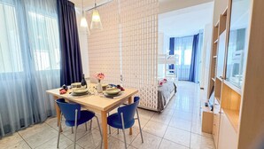 Een eethoek met een tafel voor twee, stoelen, een fles wijn en een vaas met bloemen.