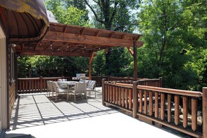 Une terrasse en bois, dotée de mobilier d’extérieur, d’une pergola et offrant une vue sur une zone boisée.
