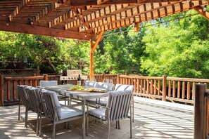 Une terrasse extérieure dotée d’une pergola en bois, d’une table avec des chaises et d’un barbecue.