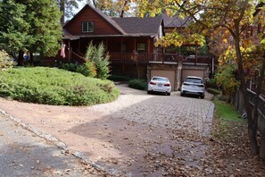 Une cabane en rondins dotée d’un porche couvert, d’un garage et d’une allée où sont garées deux voitures.