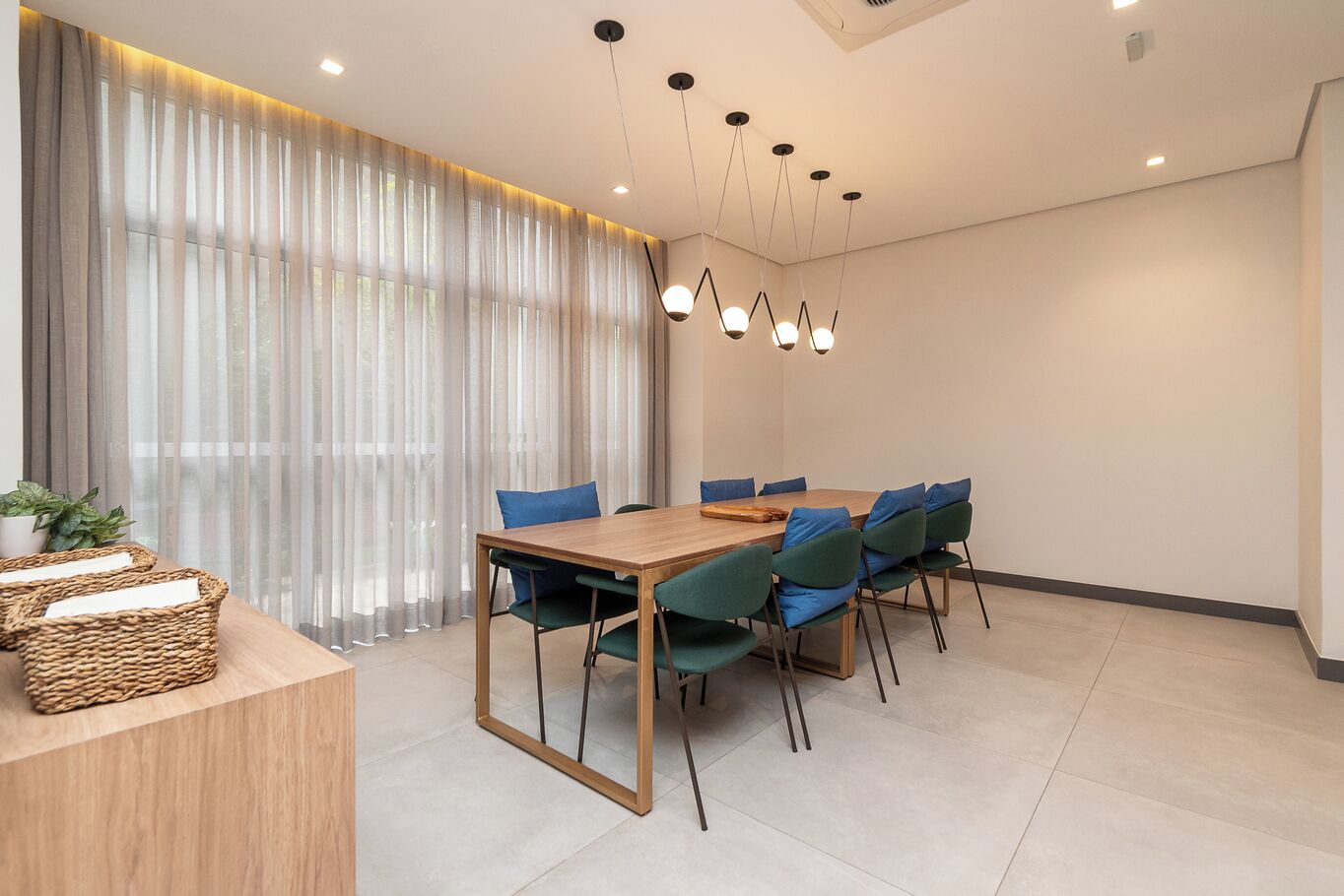 A modern dining area with a wooden table, green chairs, and a chandelier.