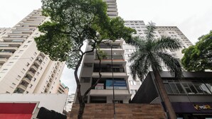 Un immeuble à plusieurs étages, avec un arbre imposant au premier plan, une enseigne indiquant « Empreendimento Lend Santa Cecília » et une devanture de magasin bien visible avec une enseigne « voa ».