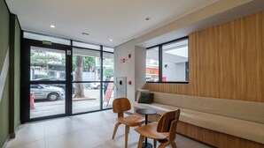 Un intérieur moderne avec un canapé, deux chaises en bois, une petite table ronde et une grande fenêtre donnant sur la rue.