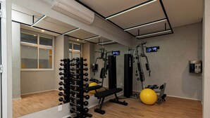 Une salle de sport équipée de matériel d’exercice, d’un banc, d’un ballon d’exercice jaune et d’une horloge numérique.