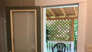 Una puerta de madera con un ventanal, que da a un porche exterior con una valla de celosía y una silla.