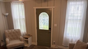 Un salón con un sillón beige, una mesita auxiliar, una puerta con un vitral y un sofá beige.