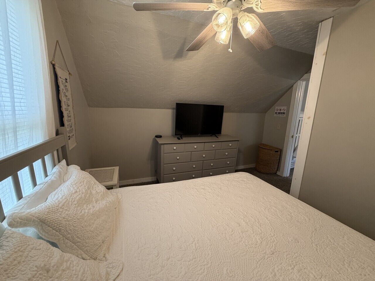 A bedroom with a bed, a dresser, a ceiling fan, and a television.