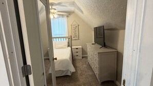 Un dormitorio con cama, cómoda, televisor y un letrero colgado en la pared.
