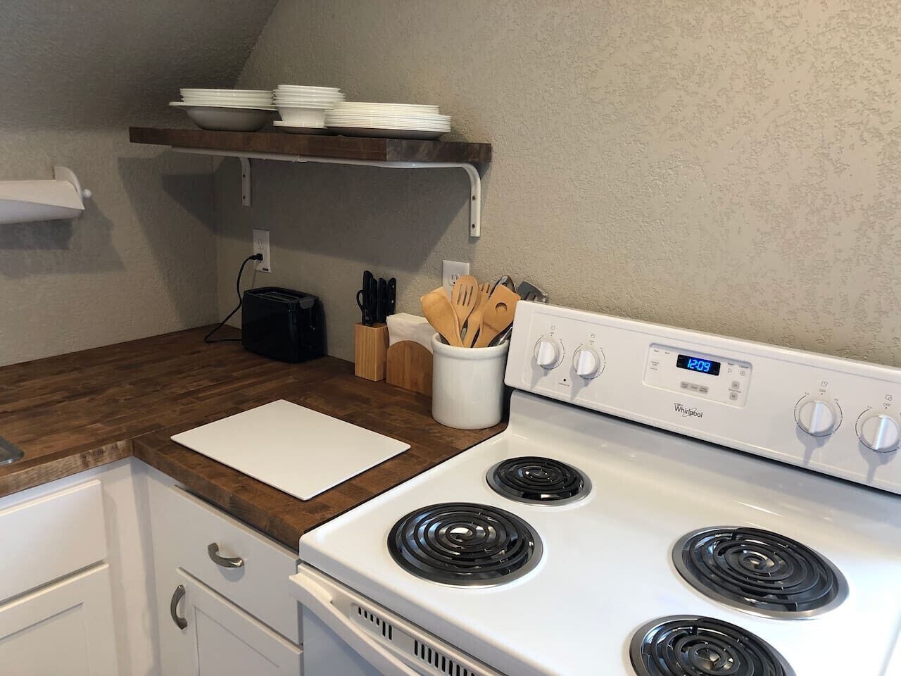 A kitchen with a white stove, wooden countertop, and a white cutting board.