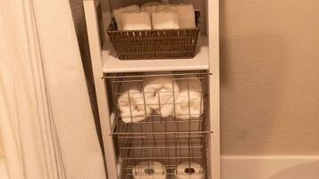 A bathroom with a white cabinet containing a wicker basket, a wire shelf with towels, and a shower curtain.
