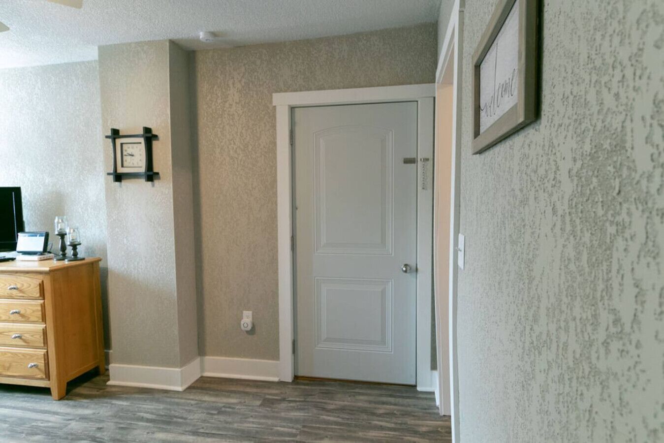 Un couloir avec une porte blanche, une commode en bois et un tableau encadré accroché au mur.