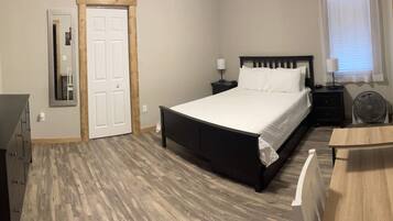 Une chambre à coucher avec un lit, des tables de chevet, un miroir, une porte et un ventilateur.