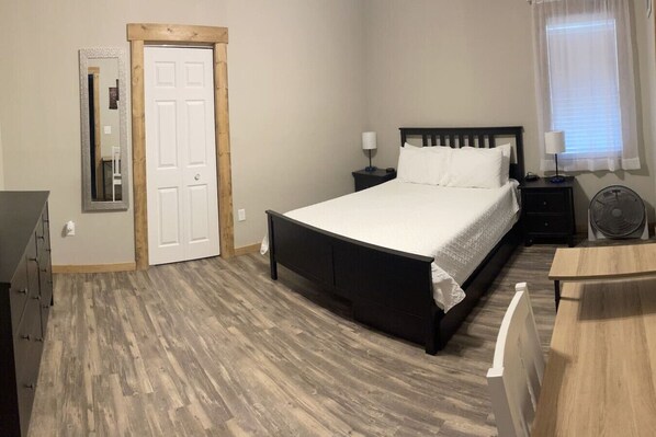 A bedroom with a bed, bedside tables, a mirror, a door, and a fan.