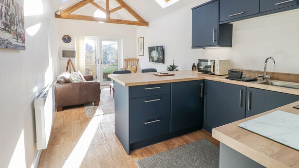 A modern kitchen with dark cabinets, a wooden countertop, and a skylight. - The Garden Cottage (Hinckley)