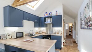 A compact kitchen with dark blue cabinets, a wooden countertop, and a skylight. - The Garden Cottage (Hinckley)