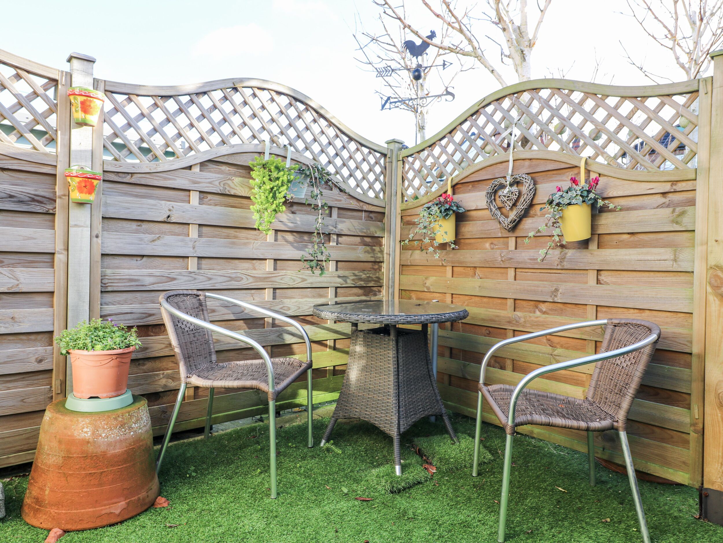 A patio area with two wicker chairs, a round table, and a wooden lattice fence.