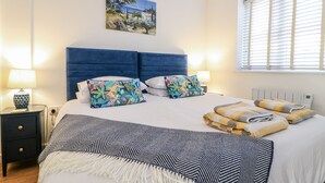 A bedroom with a large bed, two nightstands, a painting on the wall, and a window with blinds. - The Garden Cottage (Hinckley)