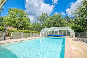 A swimming pool with a glass enclosure, surrounded by trees and a fenced area. - Girolle – Family Home with Shared Heated Pool in the Heart of the Périgord Noir (Salignac-Eyvigues)