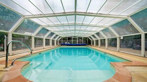 A swimming pool with a glass roof, surrounded by a tiled deck.