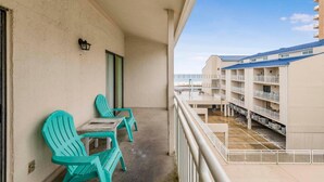 Een balkon met turquoise stoelen en een tafel, met uitzicht op een gebouw met meerdere balkons en een heldere lucht.