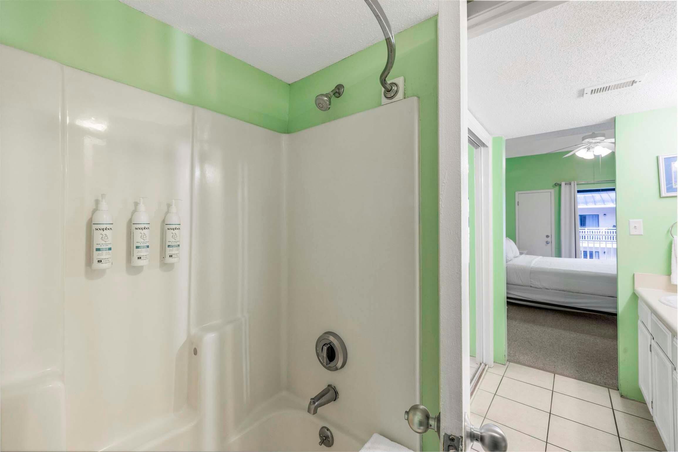 A bathroom with a shower, a toilet, and a sink. There are three bottles of shampoo on the wall.