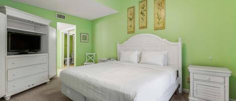 A bedroom with a bed, a dresser, a nightstand, and a television.