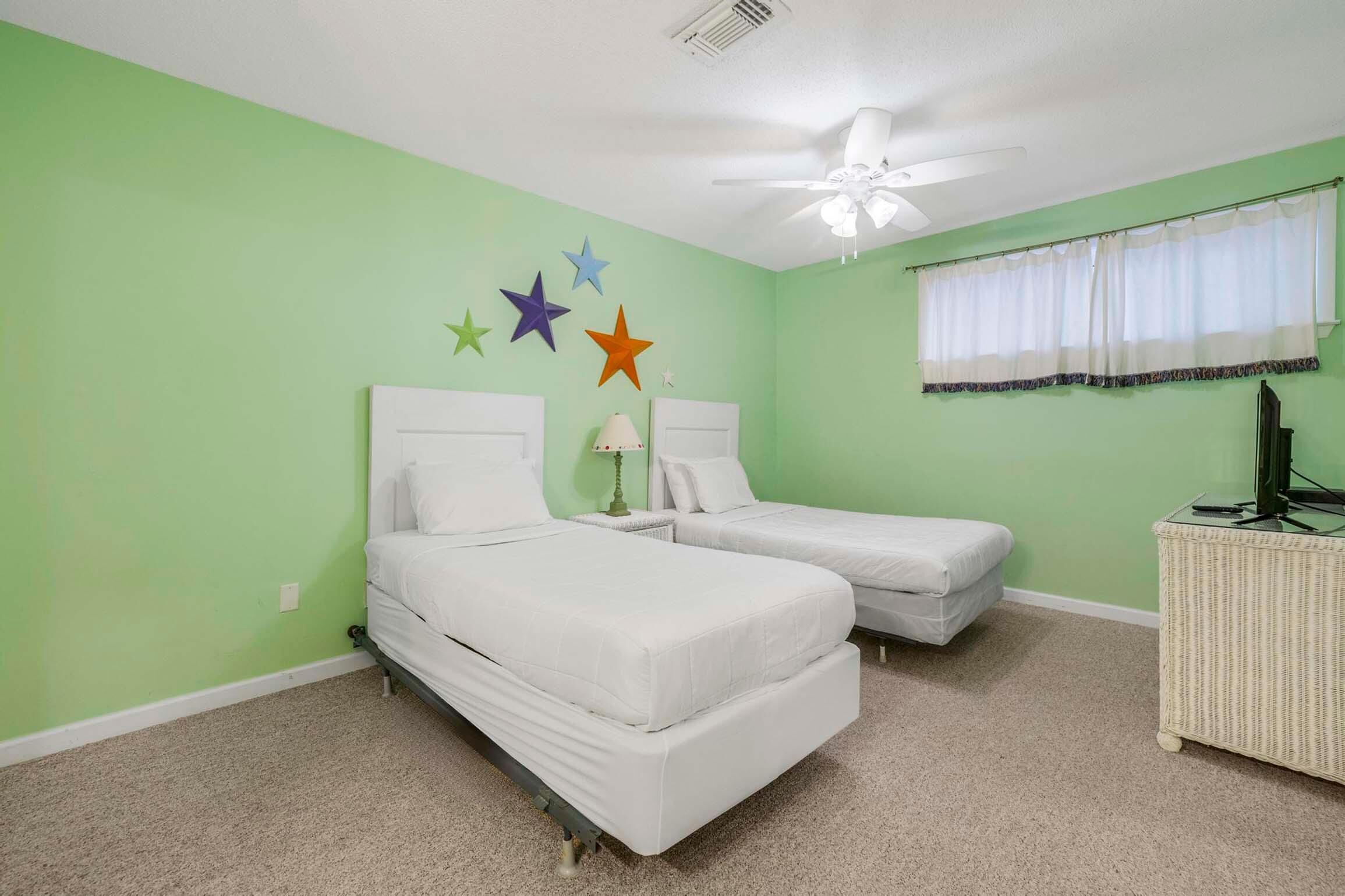 Une chambre avec deux lits, un ventilateur de plafond, une fenêtre avec un rideau et des décorations murales.