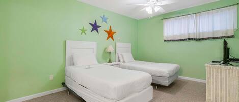 Une chambre avec deux lits, un ventilateur de plafond, une fenêtre avec un rideau et des décorations murales.