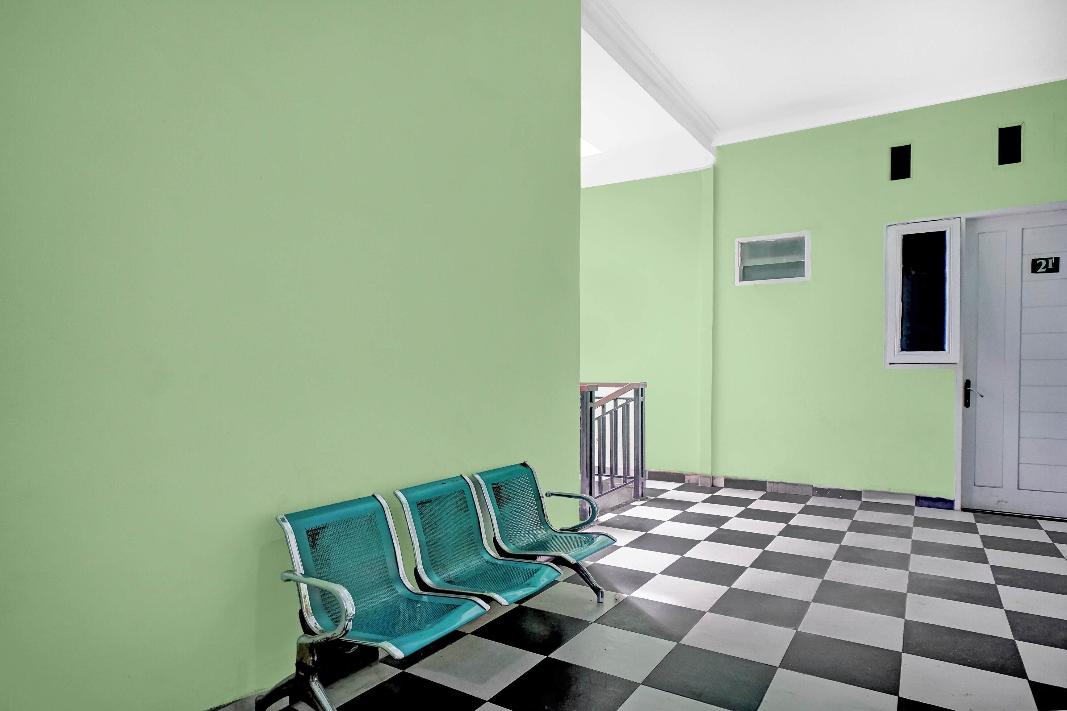 Een gang met groene wanden, een zwart-wit geruite vloer en drie groene stoelen.