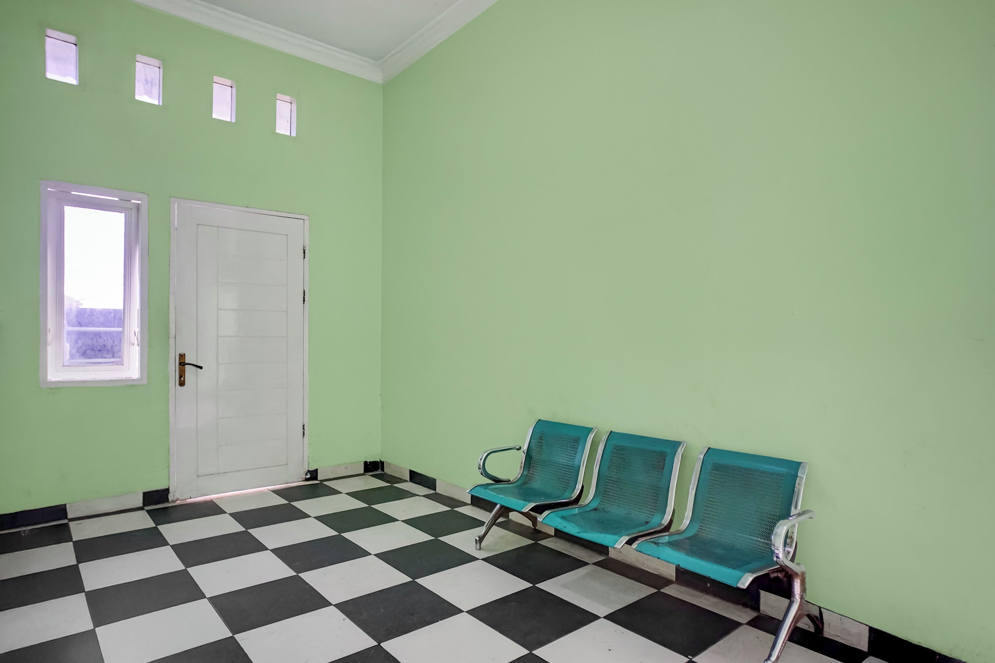 A room with a checkered floor, a white door, and three teal chairs.