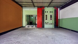 A hallway with a tiled floor, a green door, and a red pillar. - Hotel O near Universitas Medan Area (Medan)